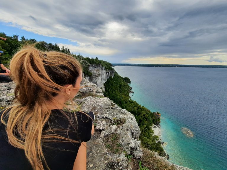 Woman sitting on cliff looking out at turquoise water