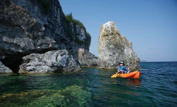 Woman kayaking in turquoise water next to rocks at the Grotto
