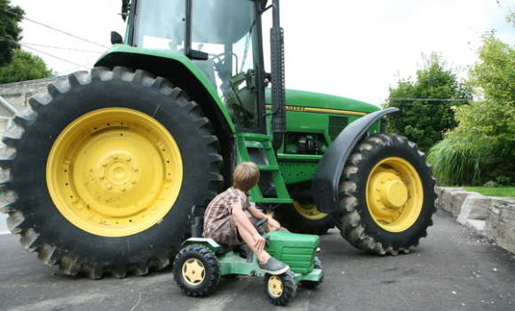 Kid on a toy green tractor next to a full size green tractor