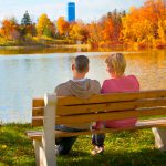 couple sitting on a bench looking out over the water, the trees are bright shades of orange