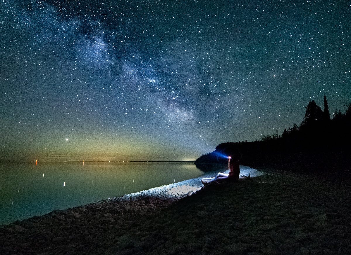 Person sitting lakeside at night looking at the milky way in the sky