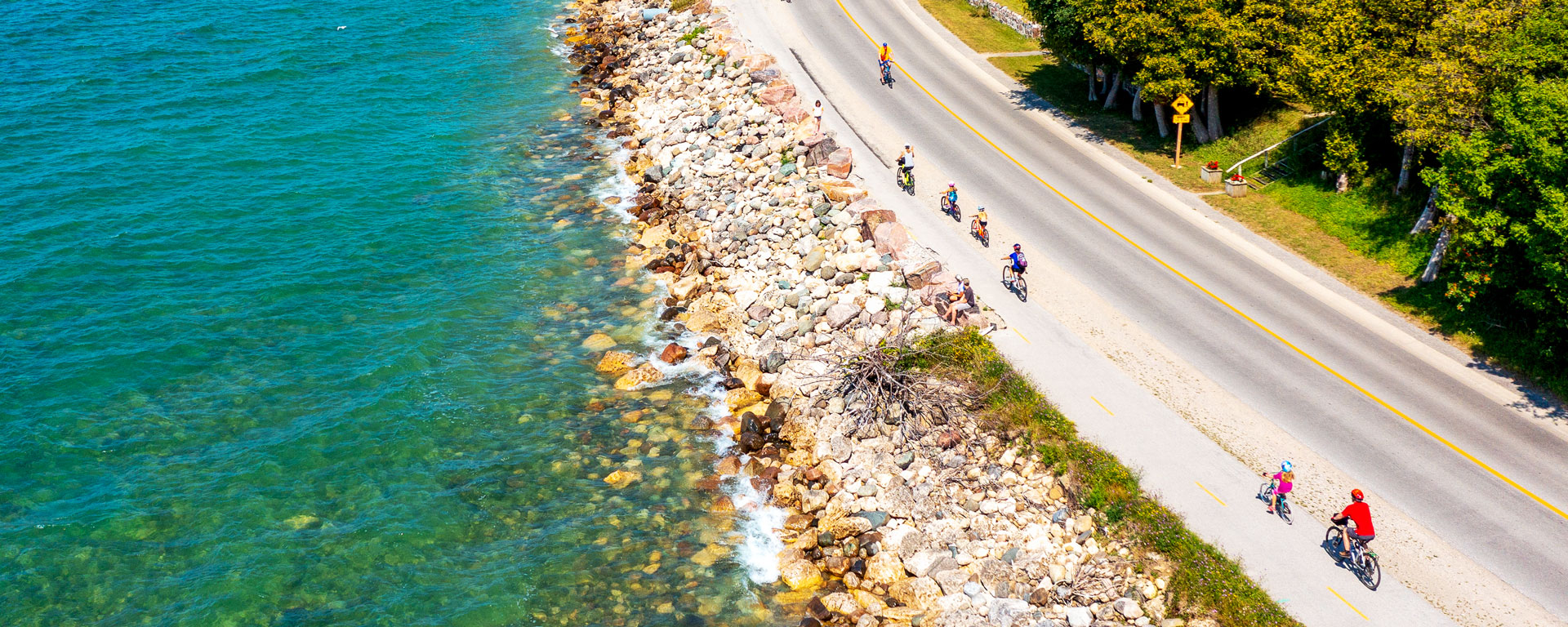 drone shot of a Group of cyclists on a road running next to a vibrant lake