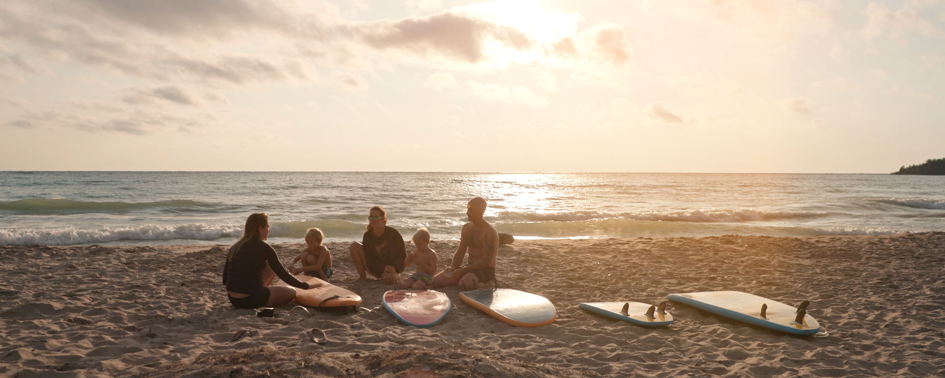 Family sitting on sandy beach with surf boards laid out around them