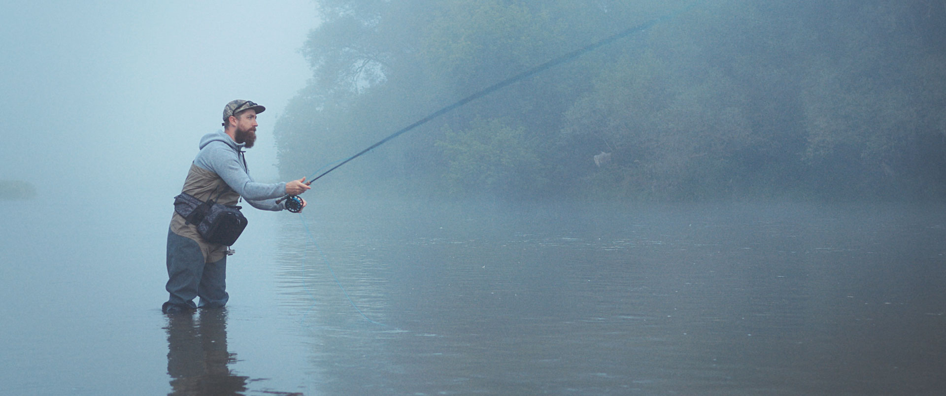 Man standing in lake fishing, in the early morning lake with mist