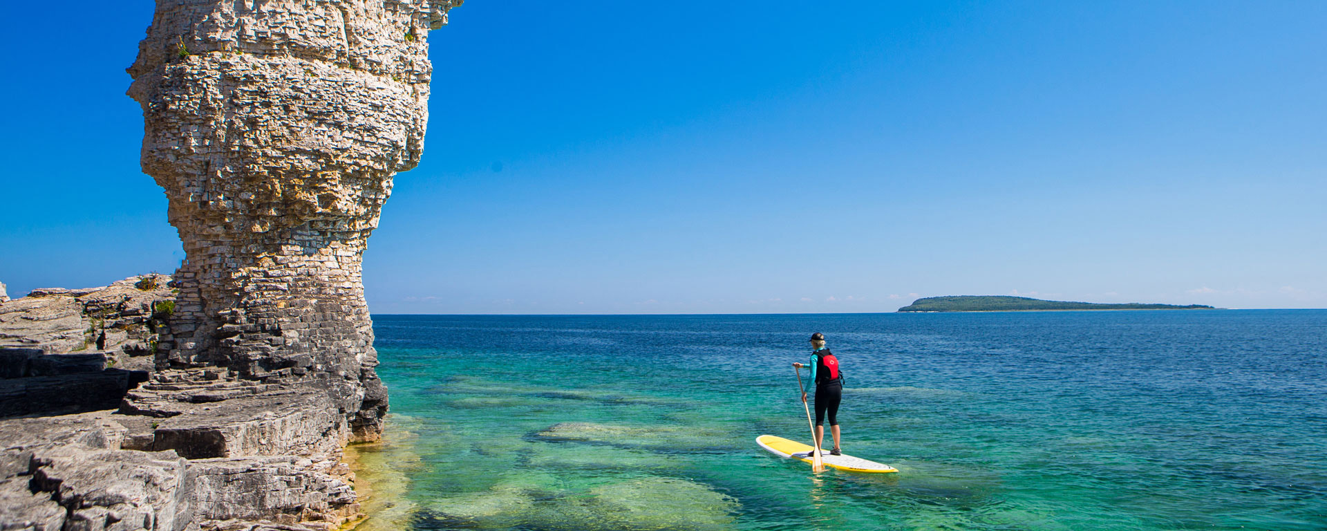 person paddle boarding near Flowerpot Island with clear blue skies