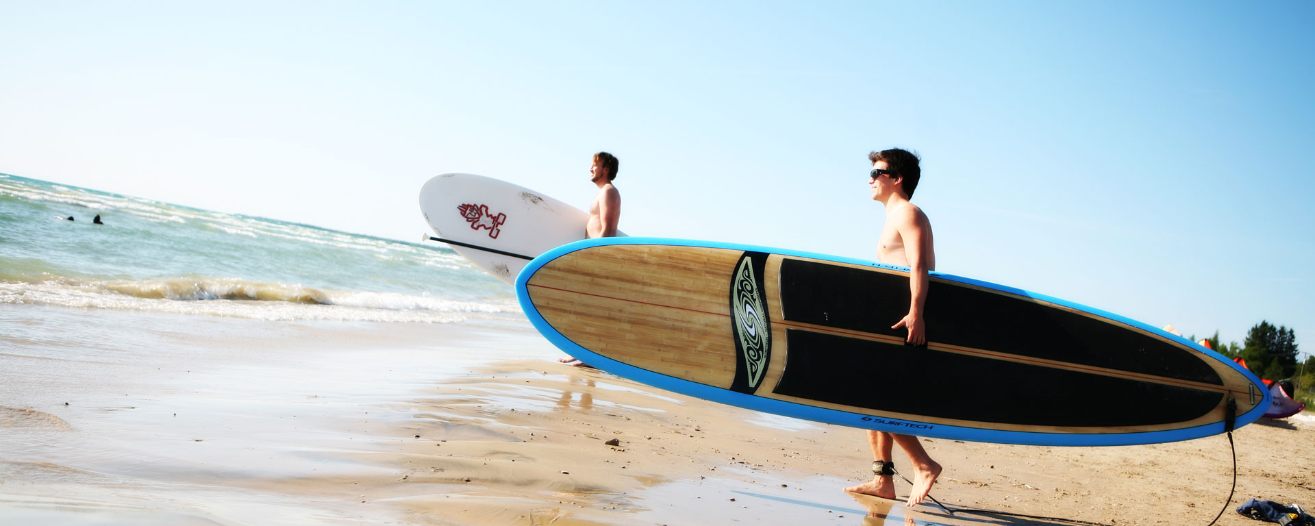two young men holding surfboards standing on a beach looking towards the water