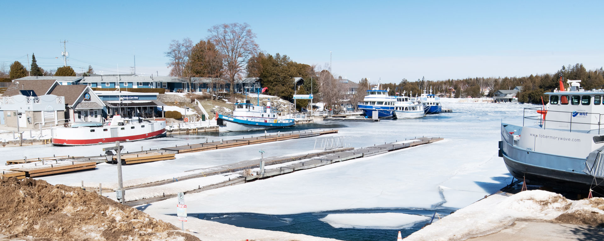 Wide shot of the marina in tobermory town. The lake is frozen over and the tree's are bare