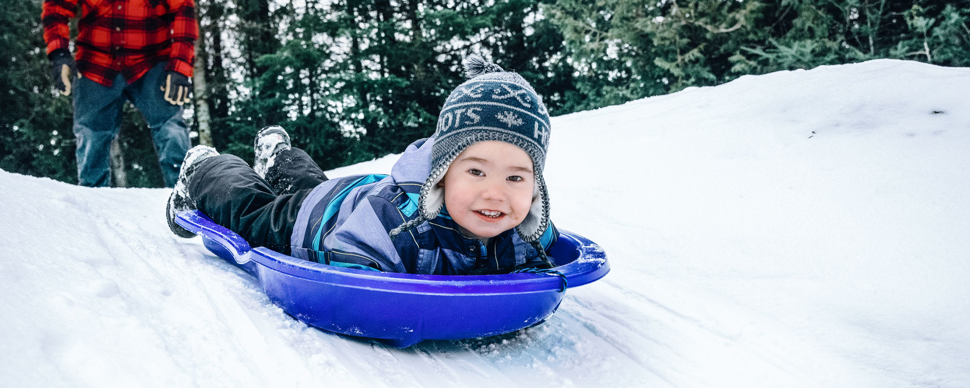 Young kid laying down in a blue sled sliding down a small hill