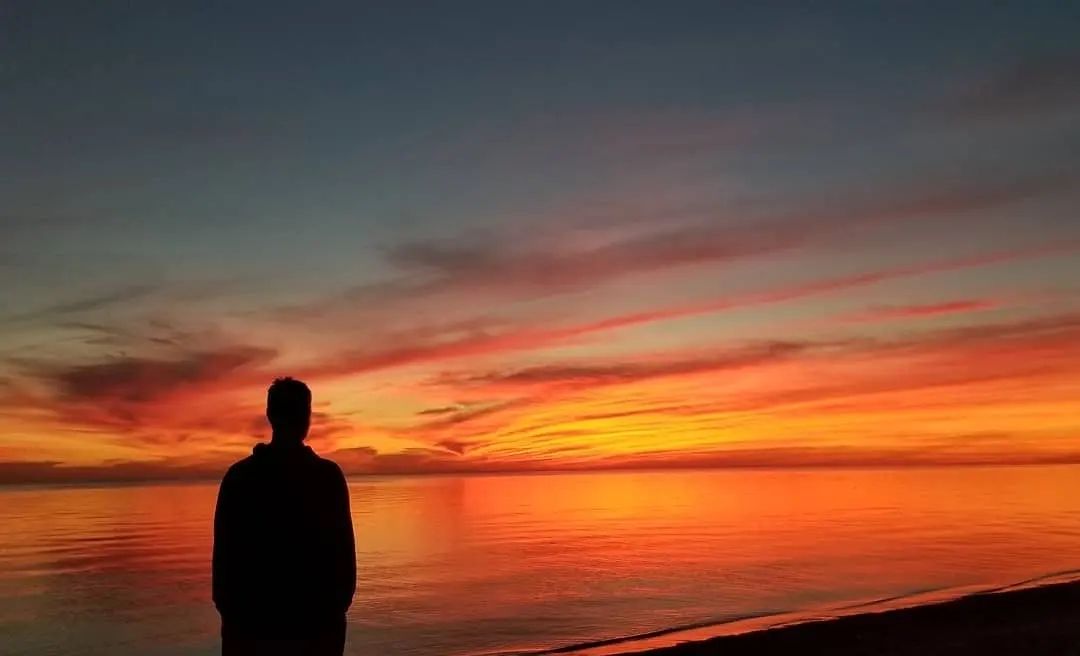 silhouette of a person staring out across the lake at a sunset the colour of fire