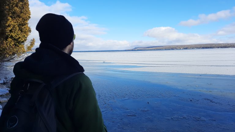 A man looking out into a bay of frozen lake water