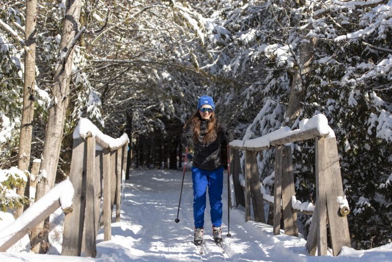 A woman cross country skiing over a wooden bridge.
