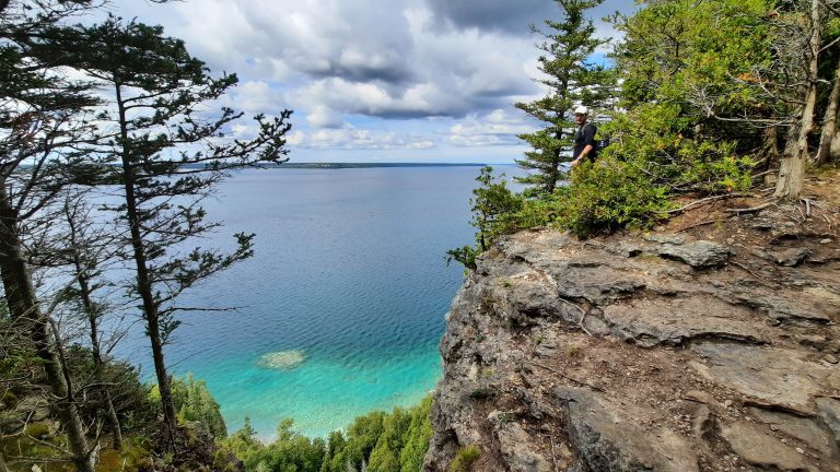 A man standing on limestone cliffs along turquoise waters of Georgian Bay